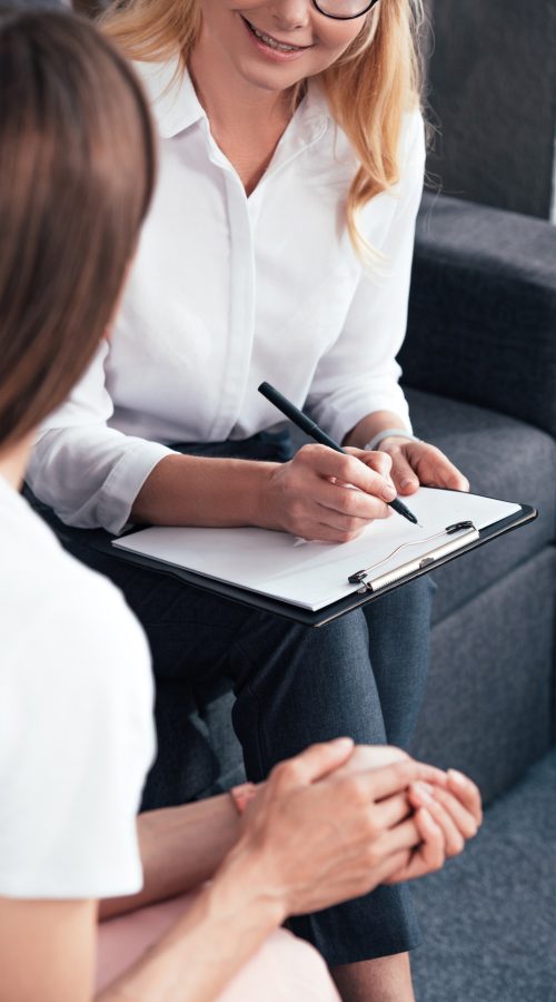 cropped image of woman talking to female counselor while she writing in clipboard at office