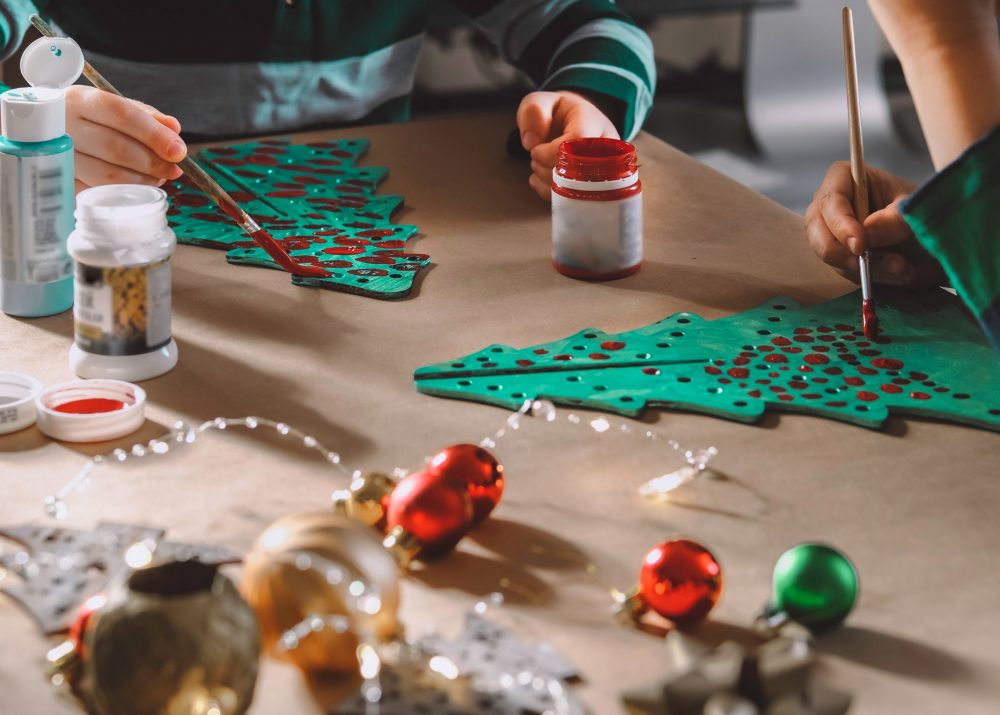 Two little kids painting wooden Christmas trees preparing holiday DIY decorations.